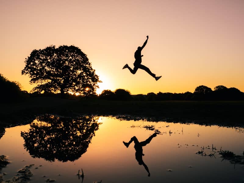 Silhouette of a person leaping over water at sunset, symbolizing forward momentum and intention