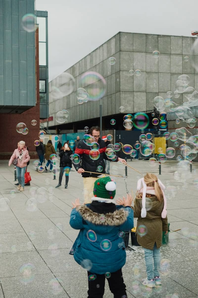 Kids reaching for floating bubbles in a city plaza, representing playfulness and presence