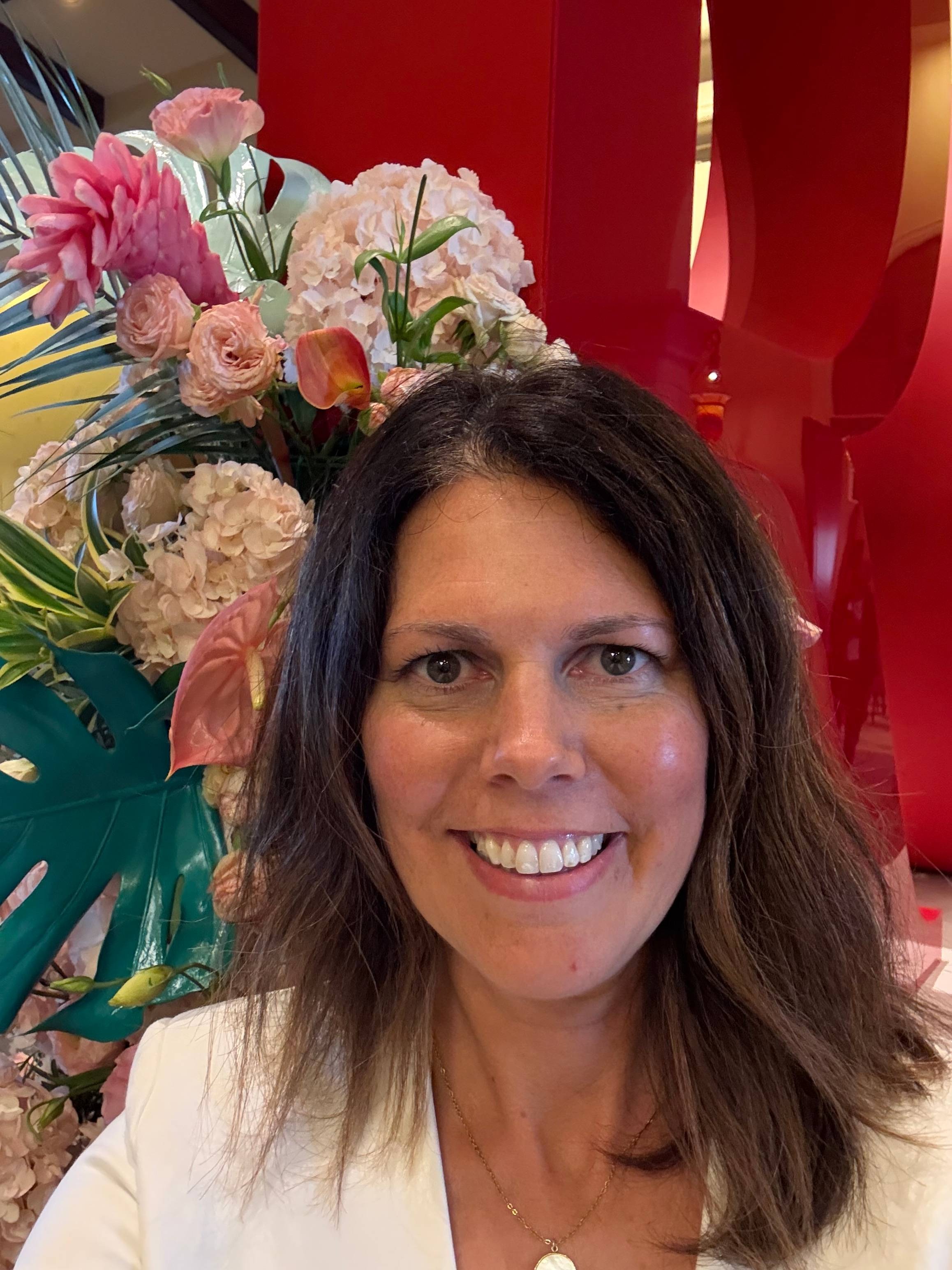 Woman smiling indoors beside large floral arrangement with red sculptural backdrop