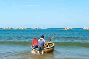 Two people pushing a small boat into the ocean, symbolizing teamwork and shared effort