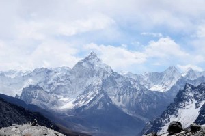 Snow-capped mountain range under a partly cloudy sky, with rocky peaks and glacial valleys stretching into the distance