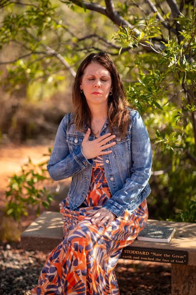 A woman sitting outdoors with her eyes closed and one hand resting on her heart during a breathwork practice